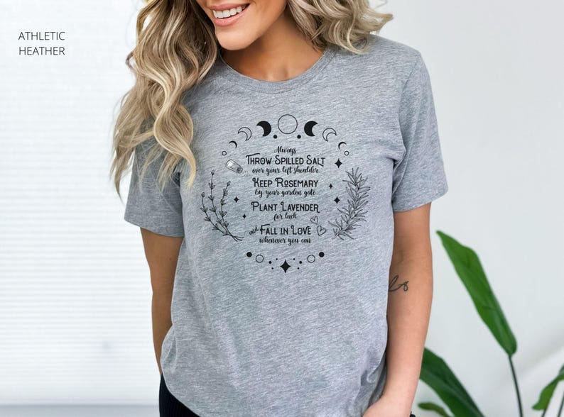 May include: Athletic heather gray t-shirt with a circular design featuring crescent moons, stars, and botanical illustrations. The text reads "Always throw spilled salt over your left shoulder, keep rosemary by your garden gate, plant lavender for luck, fall in love whenever you can."
