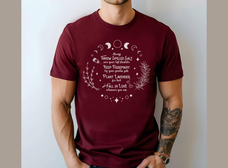 May include: A maroon t-shirt with white text and botanical illustrations. The text reads "Always throw spilled salt over your left shoulder, keep rosemary by your garden gate, plant lavender for luck, fall in love wherever you can."