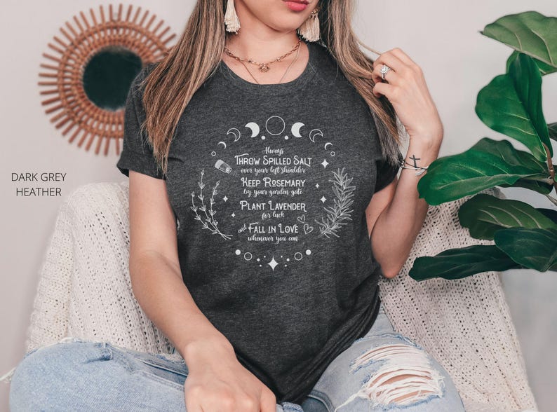 May include: Dark grey heather t-shirt with white text. The text includes phrases like "Throw spilled salt", "Keep rosemary", and "Plant lavender". The shirt is part of a spiritual or witchy theme.