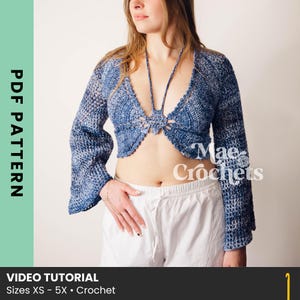May include: A blue and white crochet top with long sleeves and a plunging neckline. The top is open in the front and tied at the chest. The text "Mae & Crochets" is visible on the right side. The bottom of the image has the text "VIDEO TUTORIAL" and "Sizes XS - 5X • Crochet".