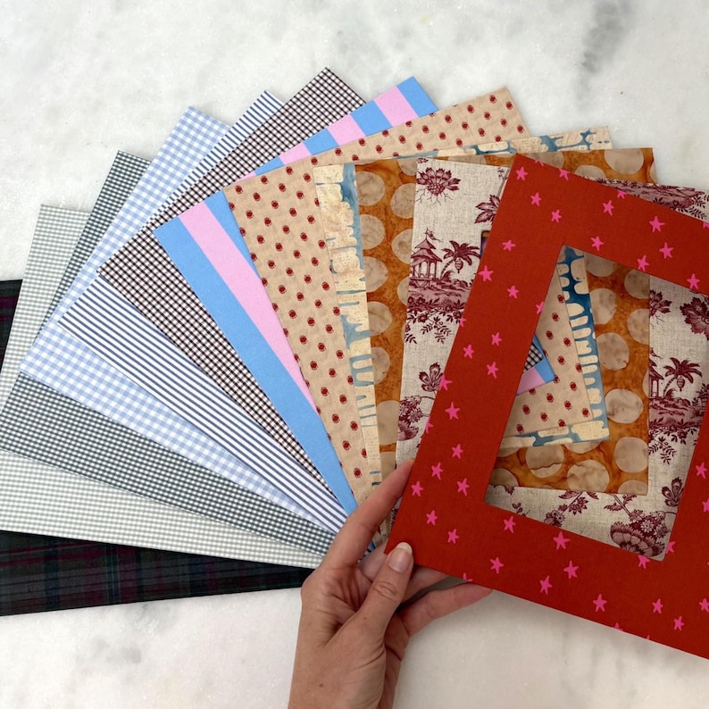 May include: A collection of rectangular fabric swatches arranged in a fan shape, featuring various patterns including gingham, stripes, polka dots, and toile. The top layer is a red fabric frame with a pink star pattern and a rectangular cutout.