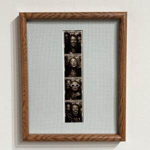 May include: A vertical photo strip featuring four black and white portraits of a person, each labeled Hotel Clermont, displayed in a rectangular wooden frame with a light green and white gingham fabric matting surrounding the central image.