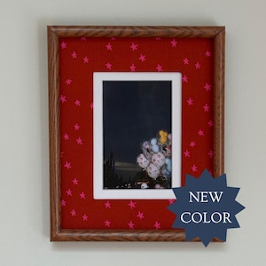 May include: A rectangular picture frame with a wood grain finish and a red mat featuring a pattern of small pink stars. The frame contains a photograph of a dark castle silhouette at night with a cluster of colorful balloons in the foreground.