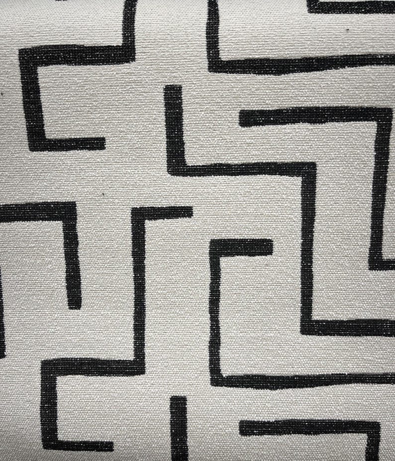 May include: Black and white geometric pattern on a white fabric background. The pattern is made up of repeating L-shaped lines.
