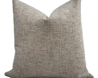 May include: A square decorative pillow with a textured woven fabric in a neutral color palette. The pillow features a grid-like pattern with shades of beige, brown, and black. The pillow is designed for home decor and adds a touch of texture.