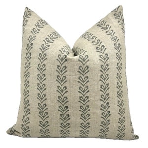 Puede incluir: Una almohada de lino beige con un patrón de hojas gris oscuro. La almohada tiene un diseño simple y moderno y agregaría un toque de sofisticación a cualquier habitación.