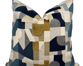 May include: A square throw pillow featuring a geometric pattern of interlocking shapes in shades of navy blue, teal, mustard yellow, light gray, and cream. The design consists of various rectangles, squares, and semi-circles with a textured fabric finish.