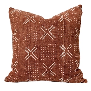 May include: A brown throw pillow with a white geometric pattern. The pattern features a series of white X's and dots.