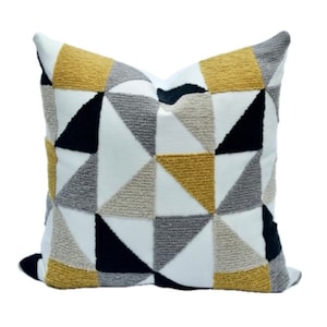 May include: A white throw pillow with a geometric pattern of black, gray, and yellow triangles. The pillow is made of a soft, textured fabric.