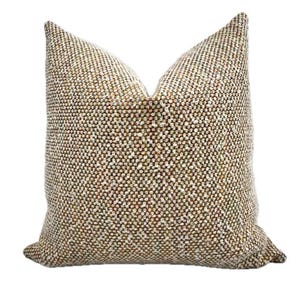 Könnte beinhalten: Ein quadratisches Zierkissen mit einem strukturierten, gewebten Stoff. Das Kissen weist eine Mischung aus Farben auf, darunter Braun, Weiß und Grün, wodurch ein gesprenkeltes Aussehen entsteht. Das Kissen ist für die Inneneinrichtung konzipiert.