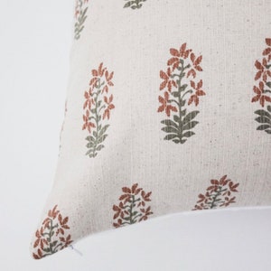 May include: A white pillow cover with a repeating pattern of rust and green floral designs.