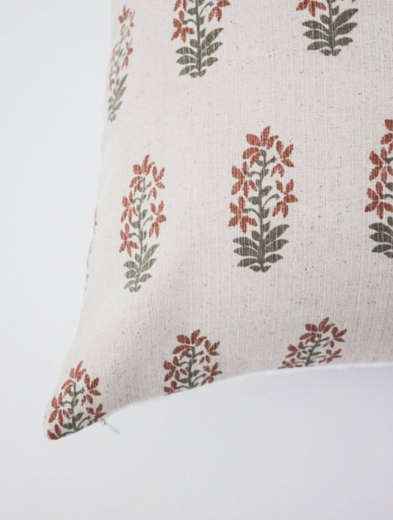 May include: A white pillow cover with a repeating pattern of rust and green floral designs.