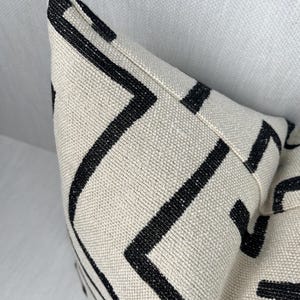 May include: A white pillow with a black geometric pattern. The pattern is made up of thin black lines that create a series of squares and rectangles.