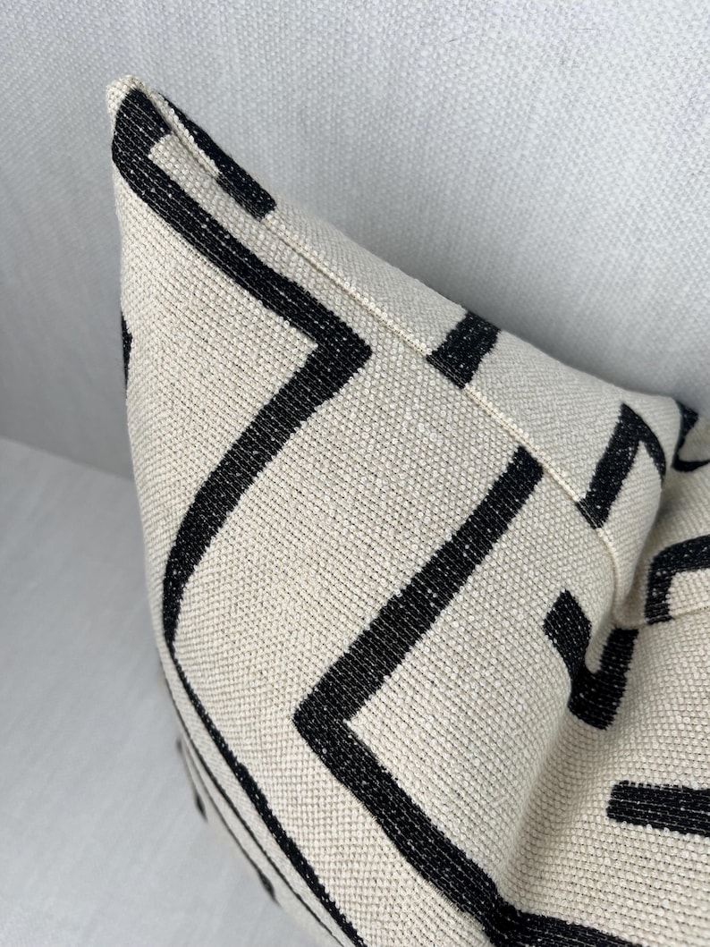 May include: A white pillow with a black geometric pattern. The pattern is made up of thin black lines that create a series of squares and rectangles.
