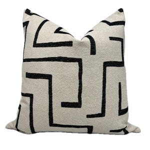 May include: A white throw pillow with a black geometric pattern. The pattern is a series of interlocking lines that create a maze-like design.