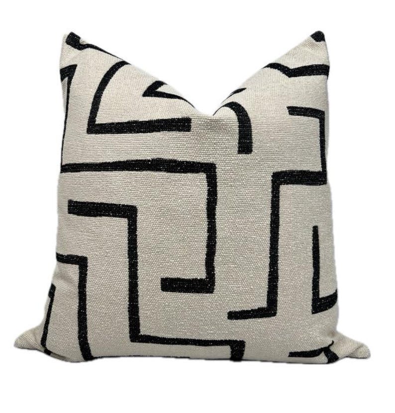 May include: A white throw pillow with a black geometric pattern. The pattern is a series of interlocking lines that create a maze-like design.