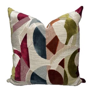 Op de afbeelding: Decoratief sierkussen met een geometrisch patchwork ontwerp. Het kussen heeft een verscheidenheid aan kleuren, waaronder bordeauxrood, blauwgroen, olijfgroen en beige. Het ontwerp bestaat uit verschillende vormen en texturen, wat een moderne en artistieke uitstraling creëert.