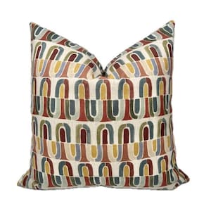 Op de afbeelding: Decoratief sierkussen met een herhalend patroon van kleurrijke, boogvormige vormen in tinten rood, groen, blauw en geel op een crèmekleurige achtergrond. Het kussen heeft een zacht, getextureerd uiterlijk, geschikt voor interieurdecoratie.