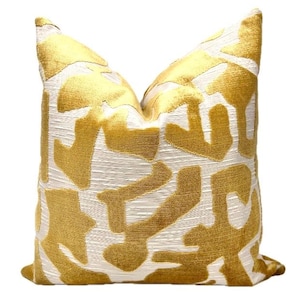 May include: A decorative throw pillow with a white background and a gold abstract pattern. The pillow is made of a soft, plush fabric.