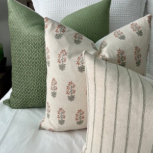 May include: Four decorative throw pillows with a white background. One pillow has a green geometric pattern, one has a green and white striped pattern, and two have a floral pattern with red and green flowers.