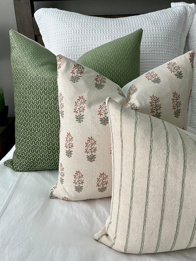 May include: Four decorative throw pillows with a white background. One pillow has a green geometric pattern, one has a green and white striped pattern, and two have a floral pattern with red and green flowers.