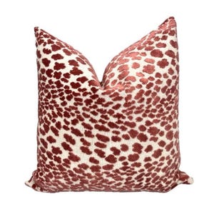 May include: A decorative throw pillow with a cream-colored background and a pattern of maroon spots. The pillow has a soft, textured appearance and is designed for home decor.