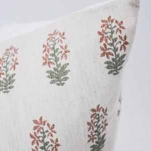 May include: A white pillow cover with a repeating pattern of rust-colored flowers with green stems and leaves.