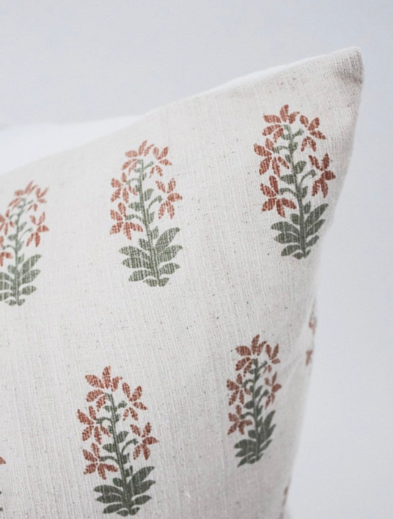 May include: A white pillow cover with a repeating pattern of rust-colored flowers with green stems and leaves.