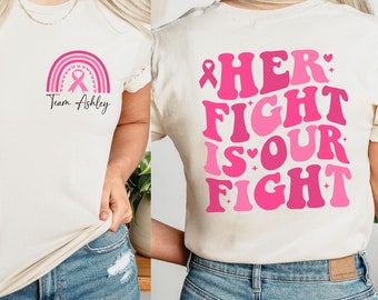 Peut inclure: Deux t-shirts blancs avec des motifs roses. Le t-shirt avant a un arc-en-ciel avec un ruban rose et le texte "Team Ashley". Le t-shirt arrière a un ruban rose et le texte "HER FIGHT IS OUR FIGHT".