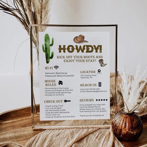 Könnte beinhalten: Ein gerahmtes Schild mit Western-Thema, auf dem das Wort "Howdy!" in goldenen Buchstaben steht. Das Schild enthält Informationen über WLAN, Hausordnung, Check-out-Anweisungen, Standort, Kontaktinformationen und Bewertungen. Das Schild ist mit einem Kaktus und einem Cowboyhut verziert.