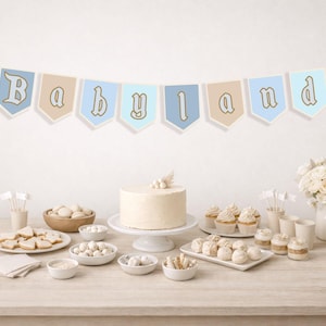 May include: A festive table setting for a baby shower, featuring a banner that reads "Babyland" with Mickey Mouse ears. The table is laden with a cake, cupcakes, cookies, and other treats, all in soft pastel colors.
