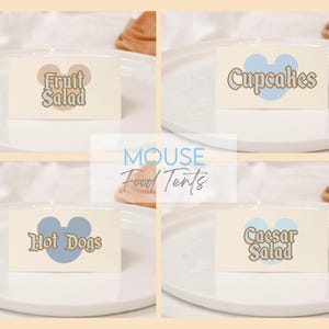 May include: Four food tent cards with the words "Fruit Salad", "Cupcakes", "Hot Dogs", and "Caesar Salad". Each card has a Mickey Mouse head shape and is on a white plate. The background is a light beige color.