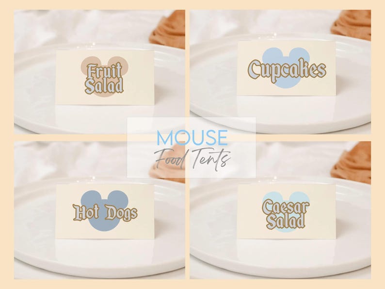 May include: Four food tent cards with the words "Fruit Salad", "Cupcakes", "Hot Dogs", and "Caesar Salad". Each card has a Mickey Mouse head shape and is on a white plate. The background is a light beige color.