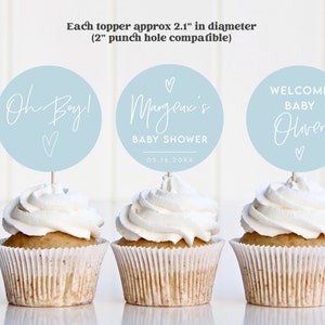 Op de afbeelding: Drie blauwe en witte cupcake-toppers met tekst die "Oh Boy!" "Margene's Baby Shower 05.16.20XX" en "Welkom Baby Oliver" luidt.