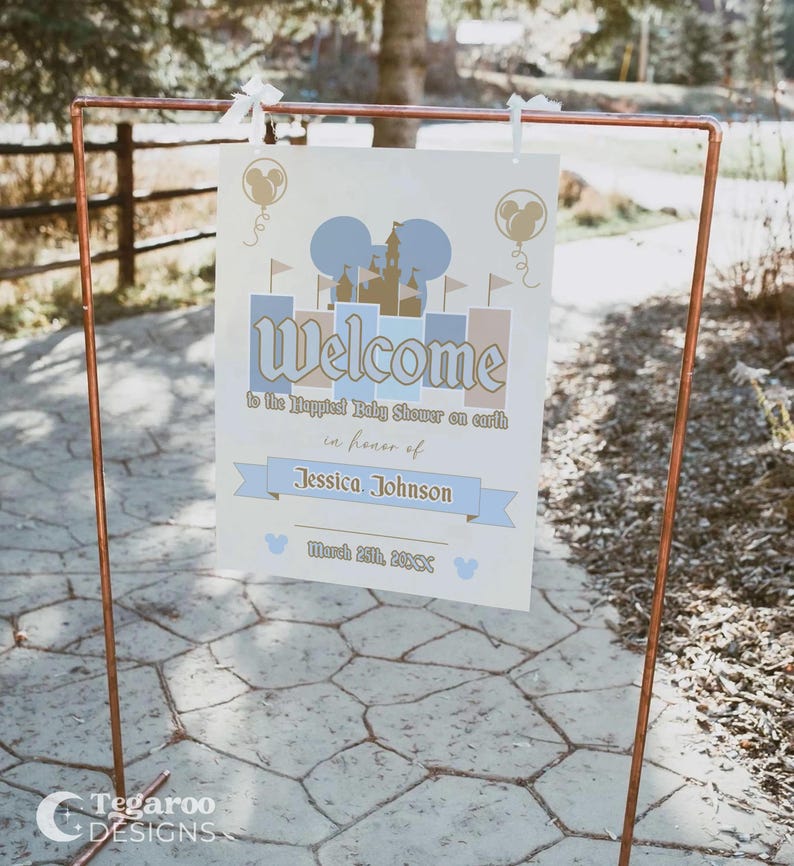 May include: A welcome sign for a baby shower, featuring a castle design and the text "Welcome to the Happiest Baby Shower on earth in honor of Jessica Johnson." The sign is displayed on a copper-colored metal stand. The date March 25th, 2018 is also included.