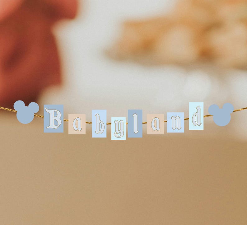 May include: A banner with the word "Babyland" spelled out in pastel-colored rectangular blocks. The letters are in a decorative font, and the banner is strung with a gold-colored string. Light blue Mickey Mouse head shapes are on each end.