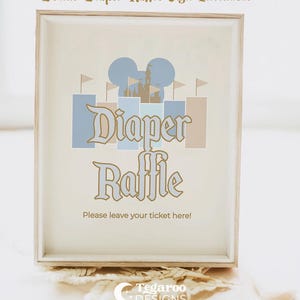 May include: Framed sign with the words "Diaper Raffle" in a decorative font, featuring a castle and Mickey Mouse ears design in blue and tan. The text "Please leave your ticket here!" is below. The sign is in a light wood frame.