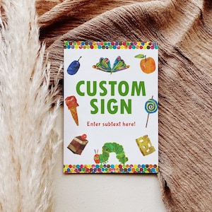 Peut inclure: Une pancarte blanche avec des illustrations color&eacute;es d'aliments et un papillon. Les mots "CUSTOM SIGN" sont en vert, avec "Enter subtext here!" en dessous. La pancarte est sur une surface marron textur&eacute;e.