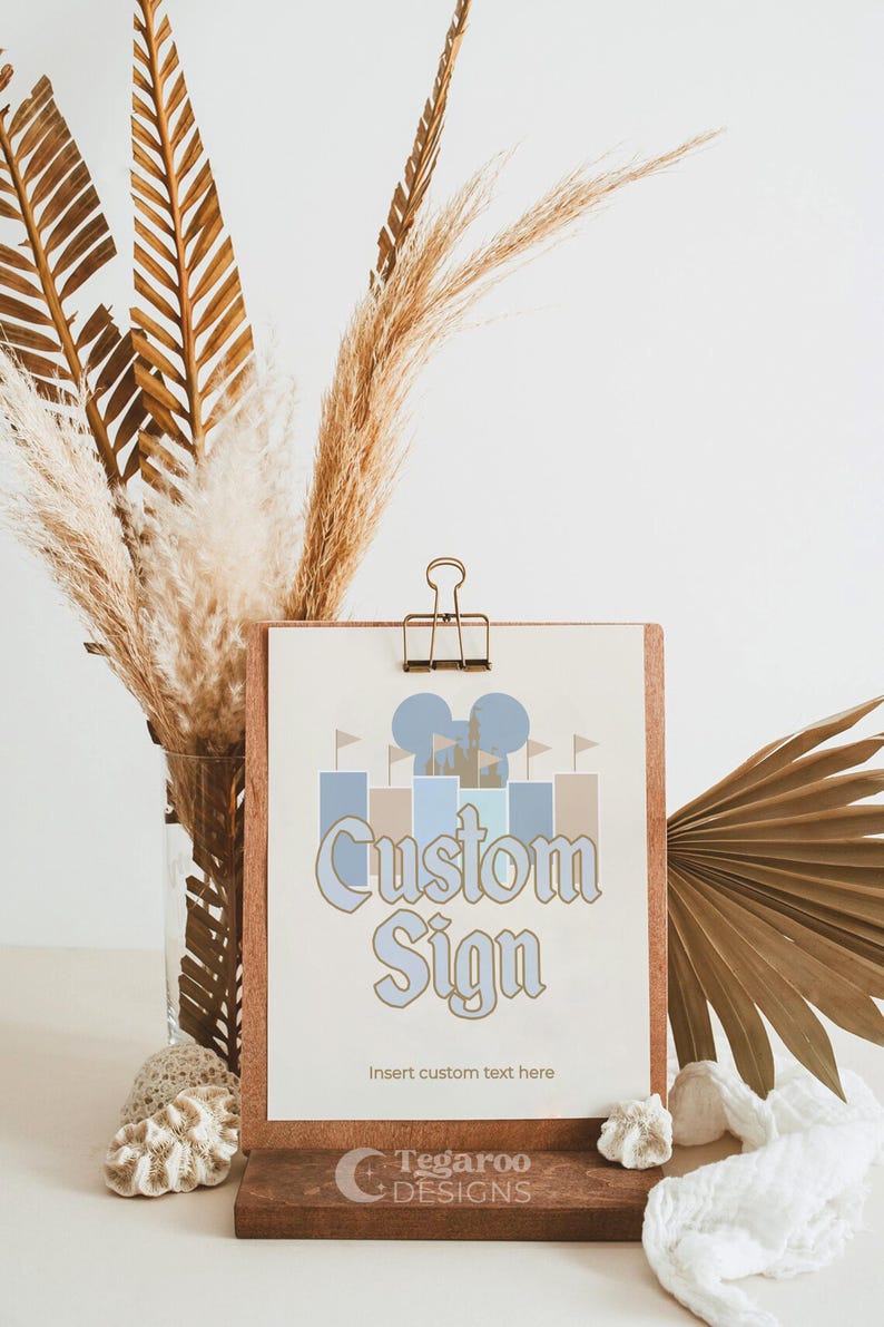 Może przedstawiać: Drukowana tabliczka z grafiką niebieskiego i brązowego zamku oraz tekstem "Custom Sign" z napisem "Insert custom text here" poniżej. Tabliczka stoi na drewnianym stojaku z napisem "Tegaroo Designs" poniżej.