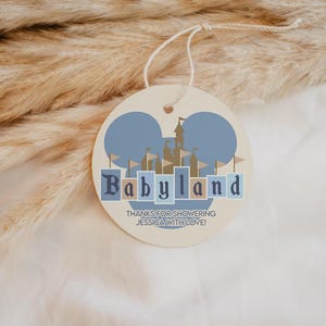 May include: A round, cream-colored tag with a blue and tan castle design and the word "Babyland" in blue letters. The tag has a string attached and the text "THANKS FOR SHOWERING JESSICA WITH LOVE!"