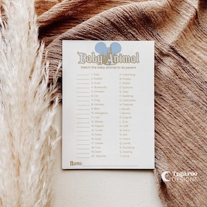 May include: A white card with the text "Baby Animal" and a matching game. The card has a list of animals and their corresponding baby names. The background is a brown fabric with a feathery plant.