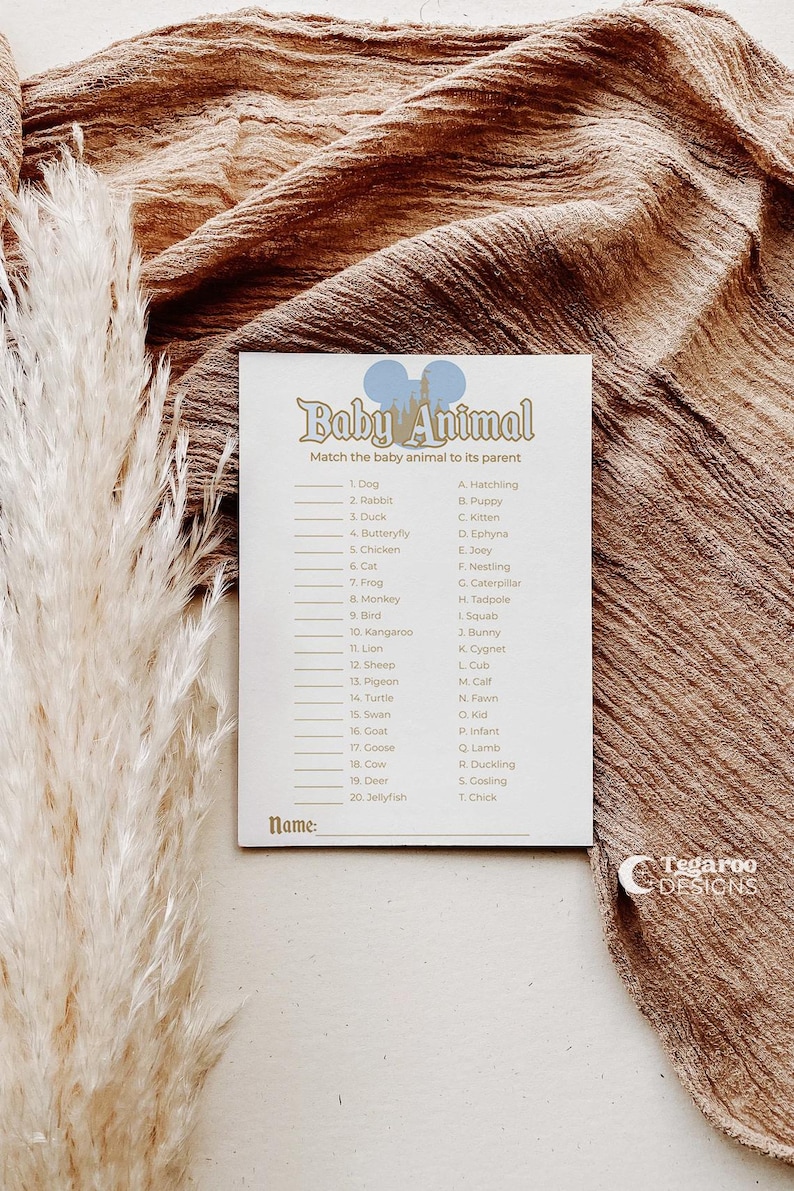 May include: A white card with the text "Baby Animal" and a matching game. The card has a list of animals and their corresponding baby names. The background is a brown fabric with a feathery plant.
