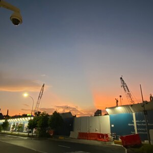 Puede incluir: Una obra en construcción al atardecer con una valla de obra azul y blanca. La valla tiene un cartel que dice "Sales Gallery Along Merchant Road, Viewing by Appointment".