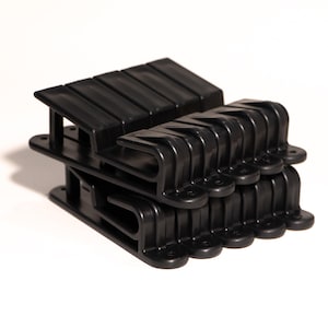 May include: A stack of black plastic clips, probably for organising or securing items. The clips are designed with a hook on one end and a flat surface on the other.