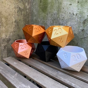 May include: Five gold, black, and white 20-sided dice planters. The dice are arranged in a semi-circle on a wooden surface.