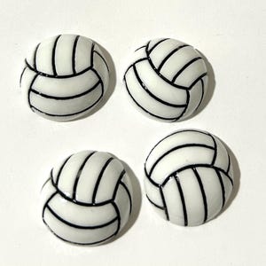 May include: Four white volleyball-themed round cabochons with black stitching.