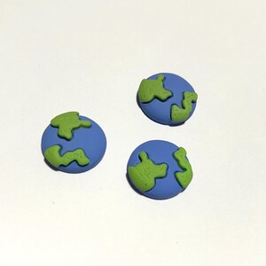 May include: Three circular buttons featuring a blue base with raised, textured green shapes representing landmasses. Each button has a smooth, matte finish and a distinct globe-like design with irregular green continents against a solid blue ocean.