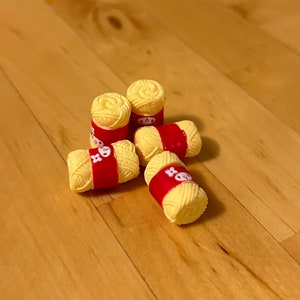Peut inclure: Cinq petites bobines de fil jaune avec des étiquettes rouges. Les bobines sont disposées en pile sur une surface en bois.