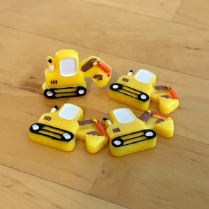 Peut inclure: Quatre véhicules de chantier en plastique jaune avec des détails noirs et bruns. Chaque véhicule a une pelle ou une pelle à l'arrière.