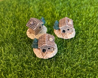 Puede incluir: Tres casas en miniatura de cerámica con techos marrones y árboles verdes, colocadas sobre un lecho de hierba artificial verde.
